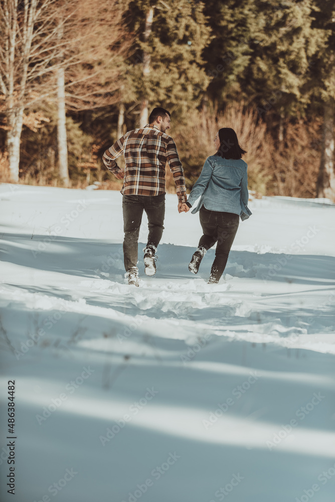 Couple running and holding hands in the winter snowy forest. Selective focus Couple running and holding hands in the winter snowy forest. Selective focus