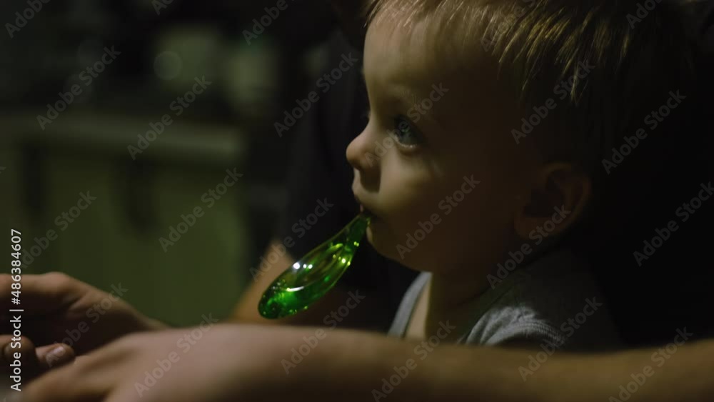 Closeup face of baby boy sits on his father's lap during dinner and watches TV. Family dinner, father and son spend time together at home.