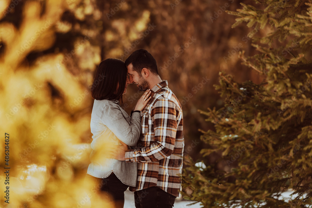 Beautiful couple hugging between snowy pines, woman in casual clothes holding hands on man chest. Selective focus
