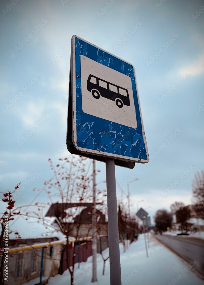 Shabby sign of bus stop on street in winter season. Road sign on blurry background. Information for people about stopping public transport.