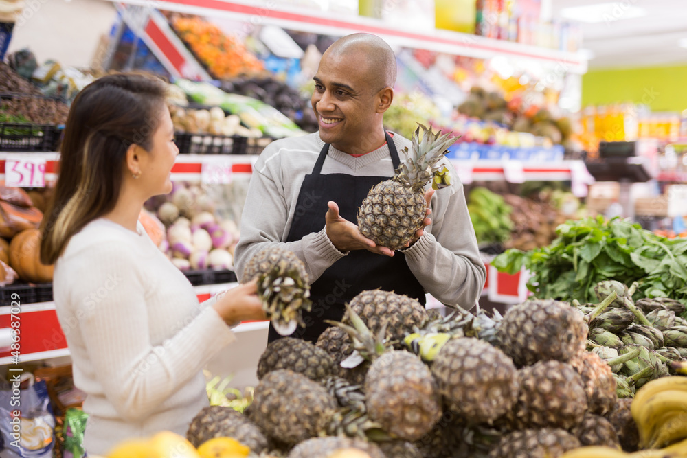 Beautiful latin woman in fruit section of supermarket with shop worker helping her