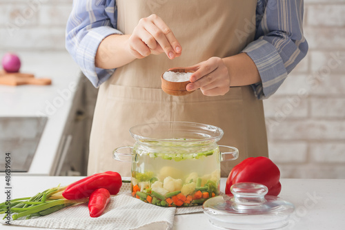 Billede på lærred Woman adding salt in tasty dietary soup on table in kitchen