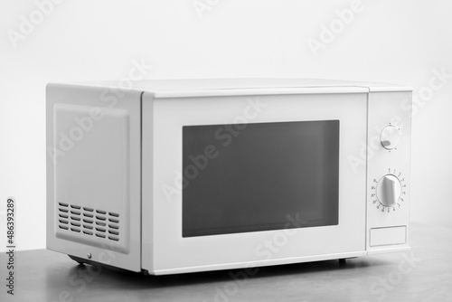 Modern microwave oven on table against light background
