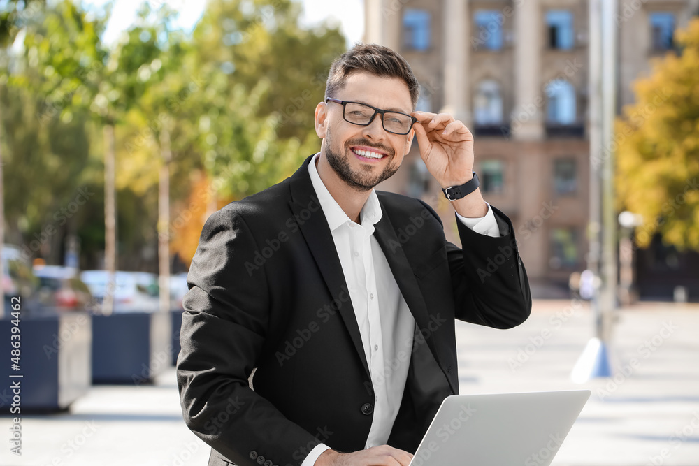Stylish businessman with laptop on city square Stylish businessman with laptop on city square