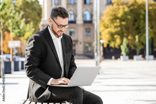 Stylish businessman working with laptop on city square