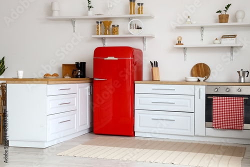 Interior of light kitchen with white counters and red fridge