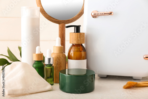 Small refrigerator with cosmetic products on light table  closeup