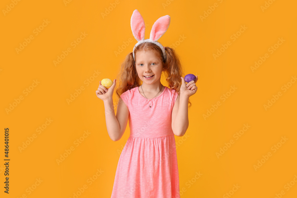 Funny little girl with bunny ears and Easter eggs on orange background