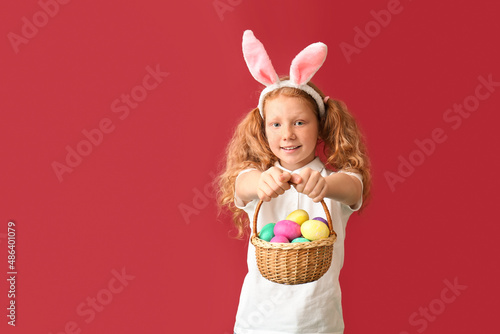 Funny little girl with bunny ears and Easter basket on red background