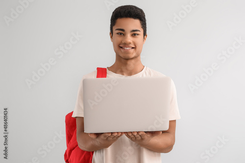 Male African-American student with backpack and laptop on light background