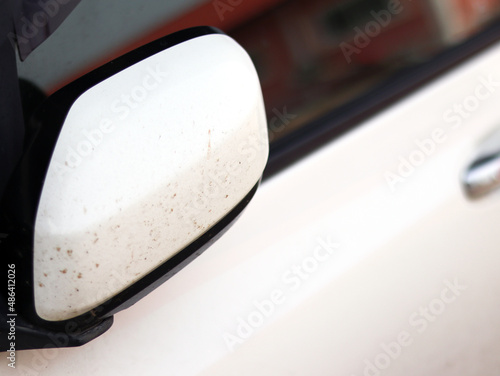 Close up White modern car strip black with rear view mirror covered with a layer of adhered dirt to a white dirty car with turn signals on the outside mirror body in the clean parking at the garage.