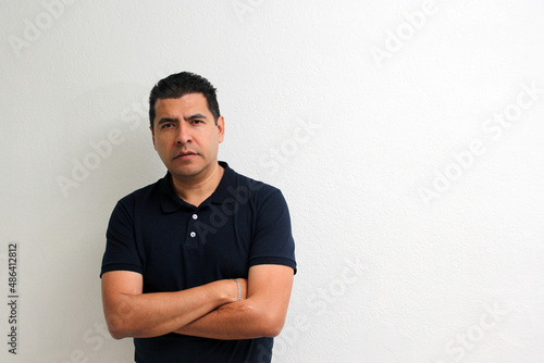 Latino adult man with short black hair and an asul navy polo shirt modeling in front of a white wall 