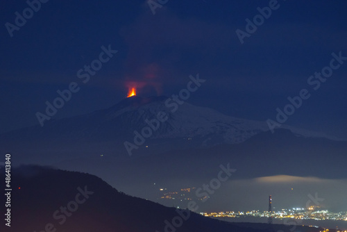 Eruption at Etna volcano at night time with sea and city lights in foreground seen from mainland on February 10 2022 , Sicily, Italy