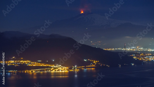 Eruption at Etna volcano at night time with sea and city lights in foreground seen from mainland on February 10 2022 , Sicily, Italy