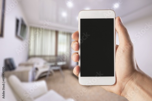 Human using smartphone, controlling smart home systems in modern apartment, blank screen