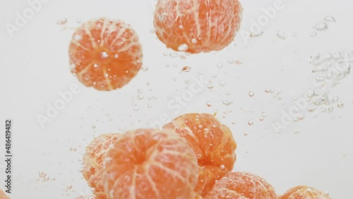 Tangerines Splashing into the Water in Slow Motion. Heap of Tangerines Falling Slowly Isolated on a White Background. Fresh water with Fruits