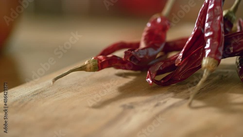 Red hot peppers pass in front of the camera in slow motion on a wooden background. Macro, 4K, Ghost Camera, Super Close Up.