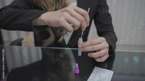 Close-up hand of Asian businesswoman uses a rapids self-test of antigens using a cotton swab to prick her nose to detect the coronavirus, COVID-19.