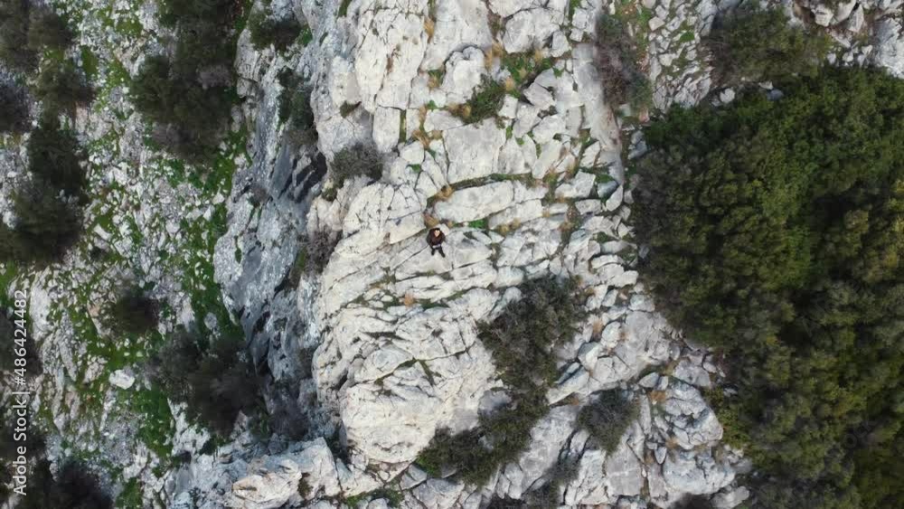 Man standing alone on rocky ledge ascending aerial topdown shot Man standing alone on rocky ledge ascending aerial topdown shot