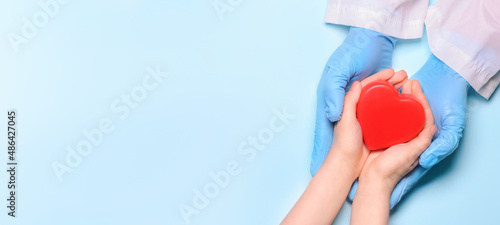 Fototapeta Naklejka Na Ścianę i Meble -  The hands of a doctor and a child hold a red heart in their hands. The concept of health, charity, organ donation. World Heart and Health Day.Copy space.