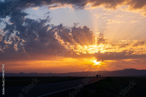 Beautiful sunset with cloudy sky and sun rays. Sunrise with road  mountains silhouettes and orange golden clouds.
