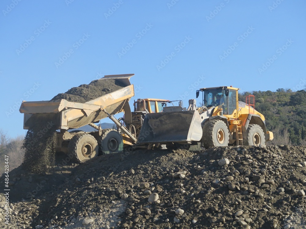 Engins de chantier jaunes pelle tracteur et camion transportant du sable et gravier pour travaux de terrassement Engins de chantier jaunes pelle tracteur et camion transportant du sable et gravier pour travaux de terrassement