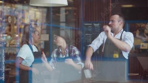 View through window of happy diverse cafe staff having fun and dancing. Realtime photo