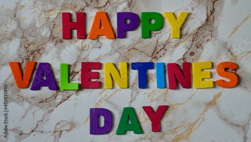 Happy Valentines Day LGBT, colored rainbow text, on marble background close up.