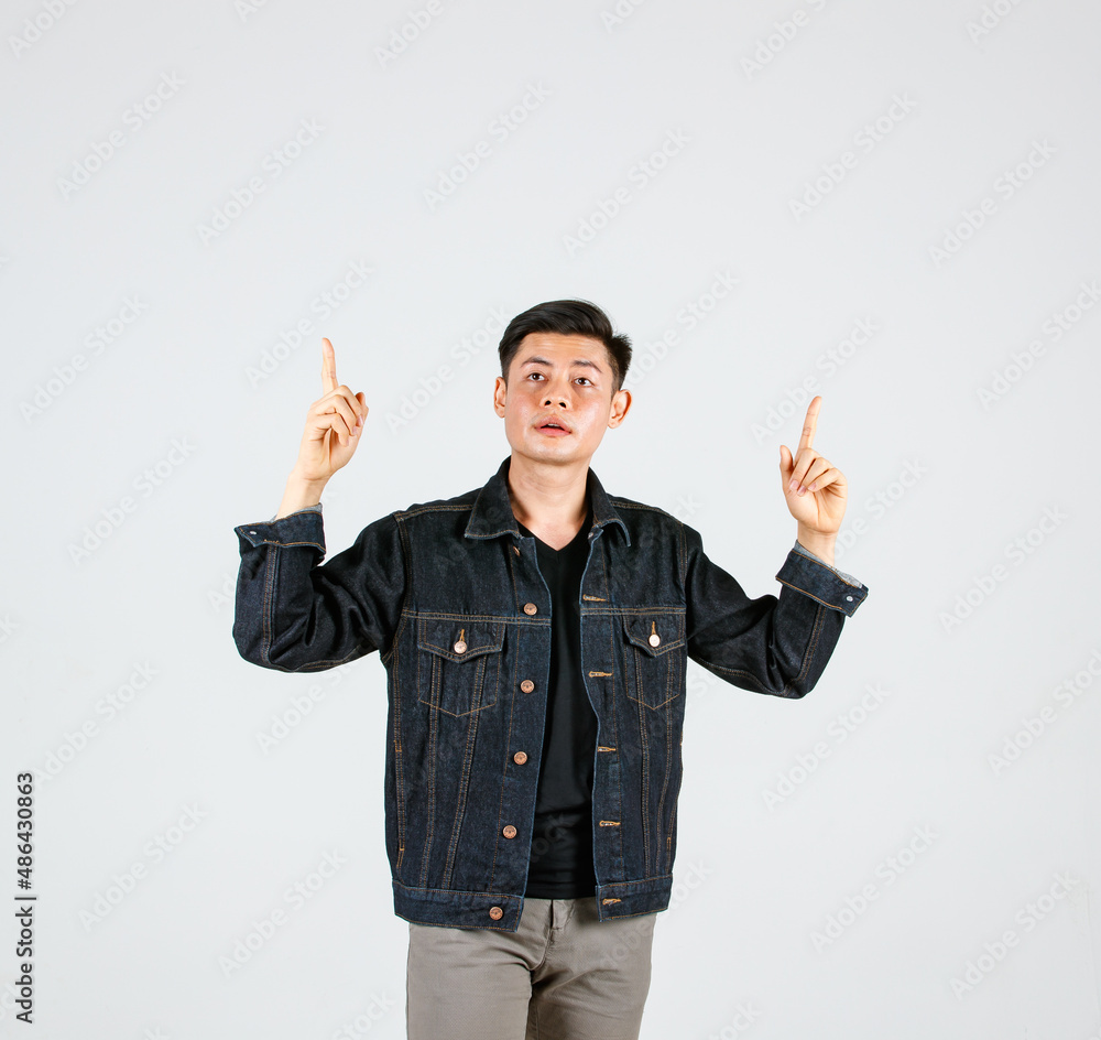 Studio shot Asian young handsome male hipster model wearing casual street denim jeans jacket standing holding hands pointing two index fingers aside presenting advertising product on gray background