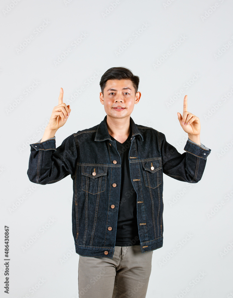 Studio shot Asian young handsome male hipster model wearing casual street denim jeans jacket standing holding hands pointing two index fingers aside presenting advertising product on gray background
