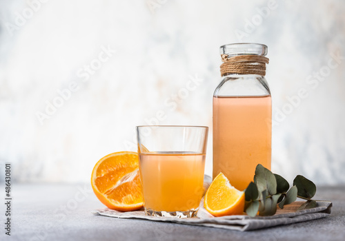 Orange lemonade in glass and bottle with fresh orange, concrete background. Refreshing summer drink. Cocktail bar background concept.