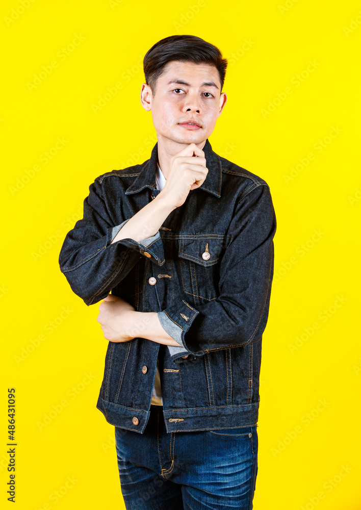 Portrait studio shot Asian young handsome male hipster model wearing casual street denim jacket jeans standing look at camera posing on yellow background. Portrait studio shot Asian young handsome male hipster model wearing casual street denim jacket jeans standing look at camera posing on yellow background.