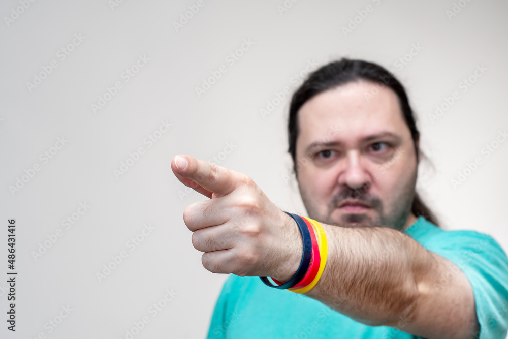 An adult, unshaven man points angrily forward. The bracelet is in the colors of the flag of Germany. Selective focus on finger. An adult, unshaven man points angrily forward. The bracelet is in the colors of the flag of Germany. Selective focus on finger.