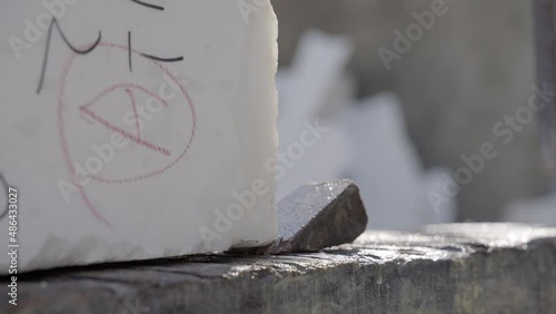 Worker Inserting Stone Wedge Under Heavy Makrana Marble Block In Open Warehouse In India. close up, slow motion photo