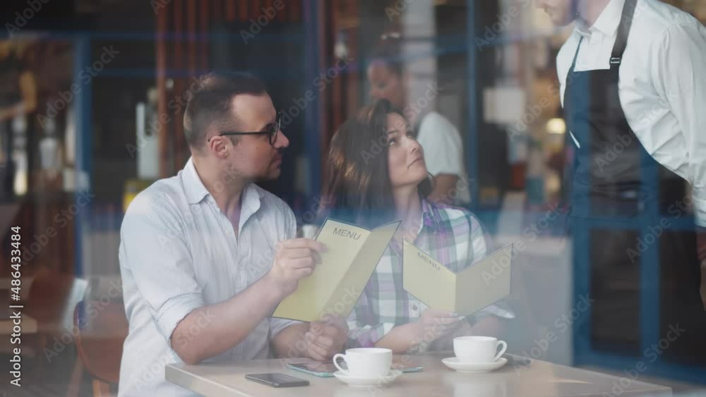 View through window of happy couple with menu order food in restaurant. Realtime View through window of happy couple with menu order food in restaurant. Realtime