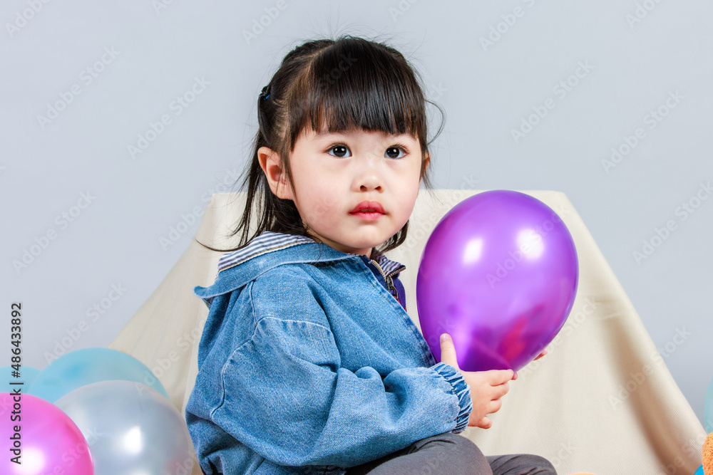 Studio shot of little cute preschooler girl daughter in casual street wears jeans jacket and sneakers sitting smiling teddy bear doll on floor playing with colorful plastic balls on gray background Studio shot of little cute preschooler girl daughter in casual street wears jeans jacket and sneakers sitting smiling teddy bear doll on floor playing with colorful plastic balls on gray background