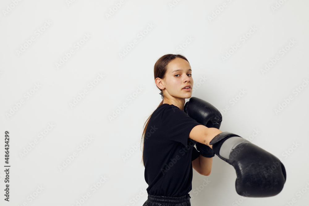 young woman in boxing gloves in black pants and a T-shirt light background young woman in boxing gloves in black pants and a T-shirt light background