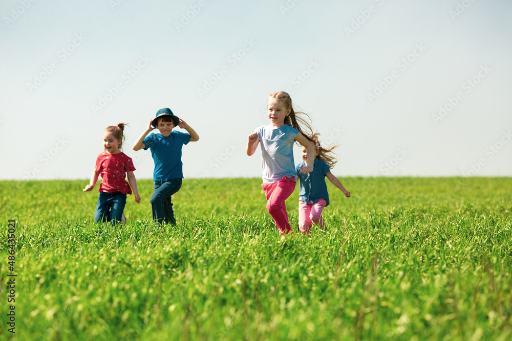 A group of happy children of boys and girls run in the Park on the grass on a Sunny summer day . The concept of ethnic friendship, peace, kindness, childhood