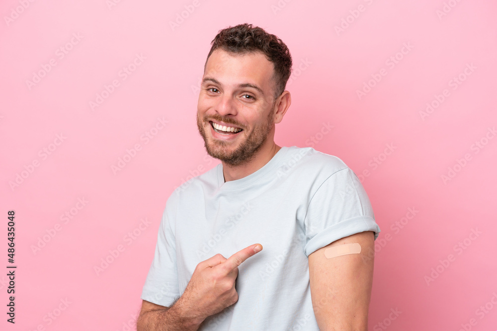 Young Brazilian man wearing a band-aids isolated on pink background and pointing it Young Brazilian man wearing a band-aids isolated on pink background and pointing it