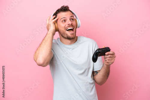 Young Brazilian man playing with video game controller isolated on pink background smiling a lot © luismolinero