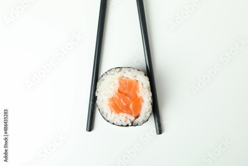 Chopsticks with maki on white background, close up