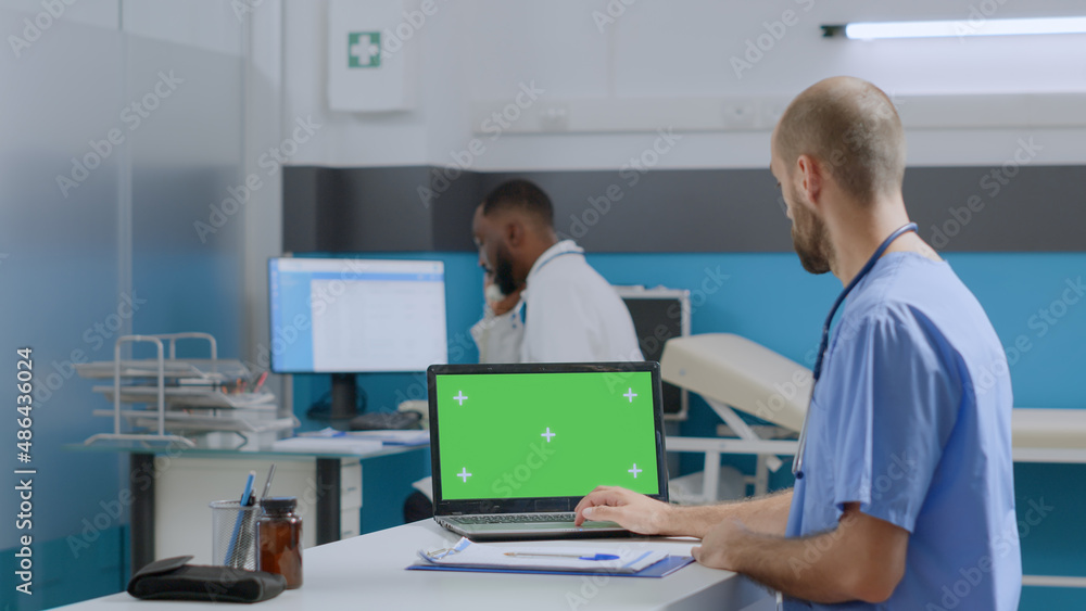 Therapist man nurse sitting at desk typing sickness expertise on mock up green screen chroma key laptop computer with isolated display. Multi-ethnic team working at healthcare treatment Therapist man nurse sitting at desk typing sickness expertise on mock up green screen chroma key laptop computer with isolated display. Multi-ethnic team working at healthcare treatment