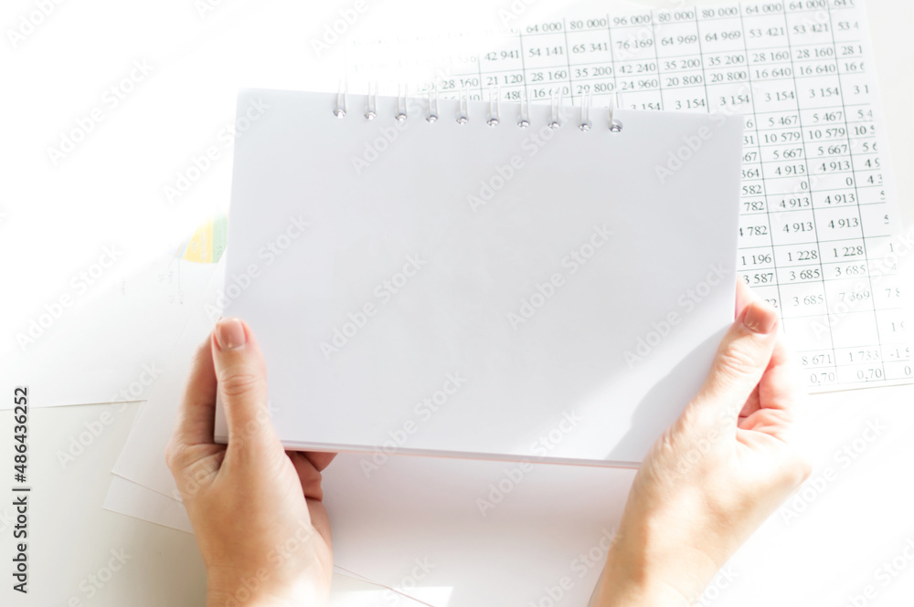 on the background of the table, the girl's hands hold a notebook, empty for writing down the text on the background of the table, the girl's hands hold a notebook, empty for writing down the text