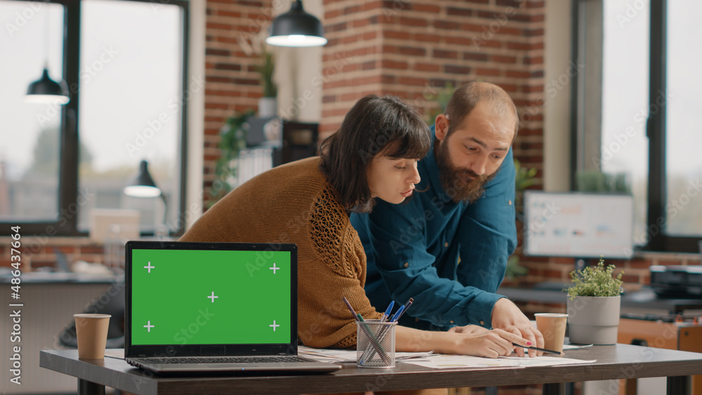 Colleagues working and having laptop with green screen on display in startup office. Business people designing project strategy while having chroma key and isolated mockup template. Colleagues working and having laptop with green screen on display in startup office. Business people designing project strategy while having chroma key and isolated mockup template.