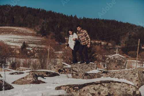 Beautiful couple in winter nature walking the rocks covered by snow, against a cloudless sky and bare trees. Selective focus. photo