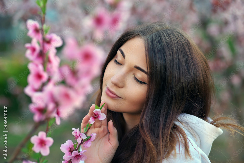 Smiling beautiful girl standing near a peach tree during sunset. Happy face. Spring time.