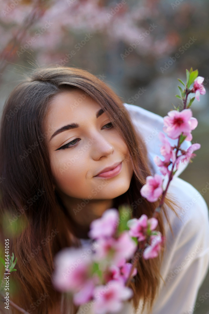 Smiling beautiful girl standing near a peach tree during sunset. Happy face. Spring time. Smiling beautiful girl standing near a peach tree during sunset. Happy face. Spring time.