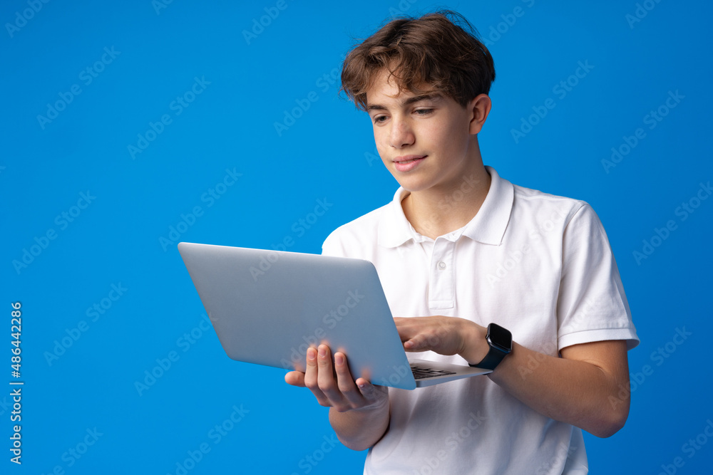 Teenage boy using laptop against blue background Teenage boy using laptop against blue background