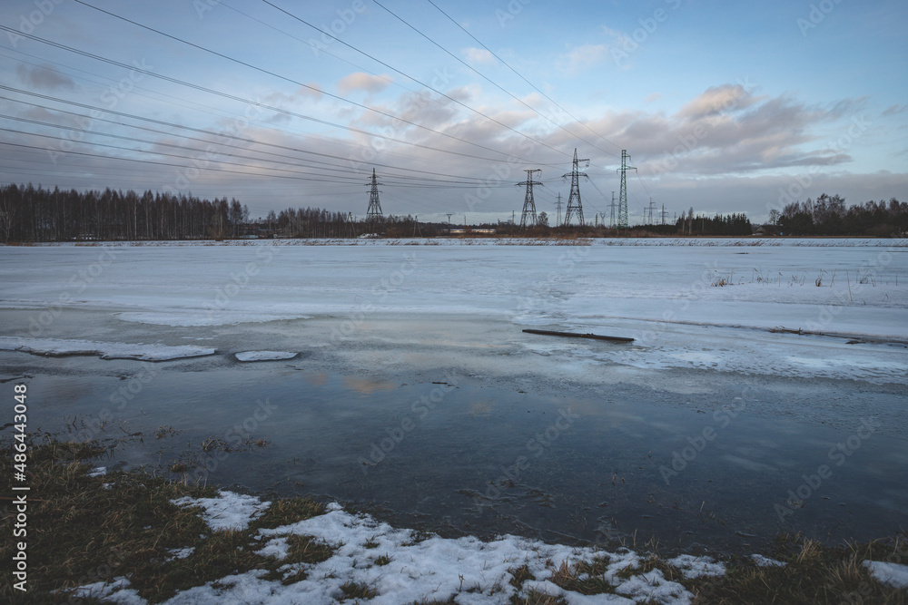 high voltage electric power lines in flood region, Jelgava, Latvia, melting snow, blue sky with fluffy clouds, evening light, reflection of pylons