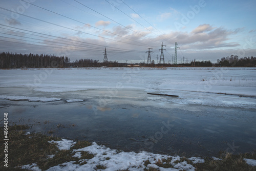 high voltage electric power lines in flood region, Jelgava, Latvia, melting snow, blue sky with fluffy clouds, evening light, reflection of pylons photo